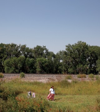 Woman in field near train tracks.