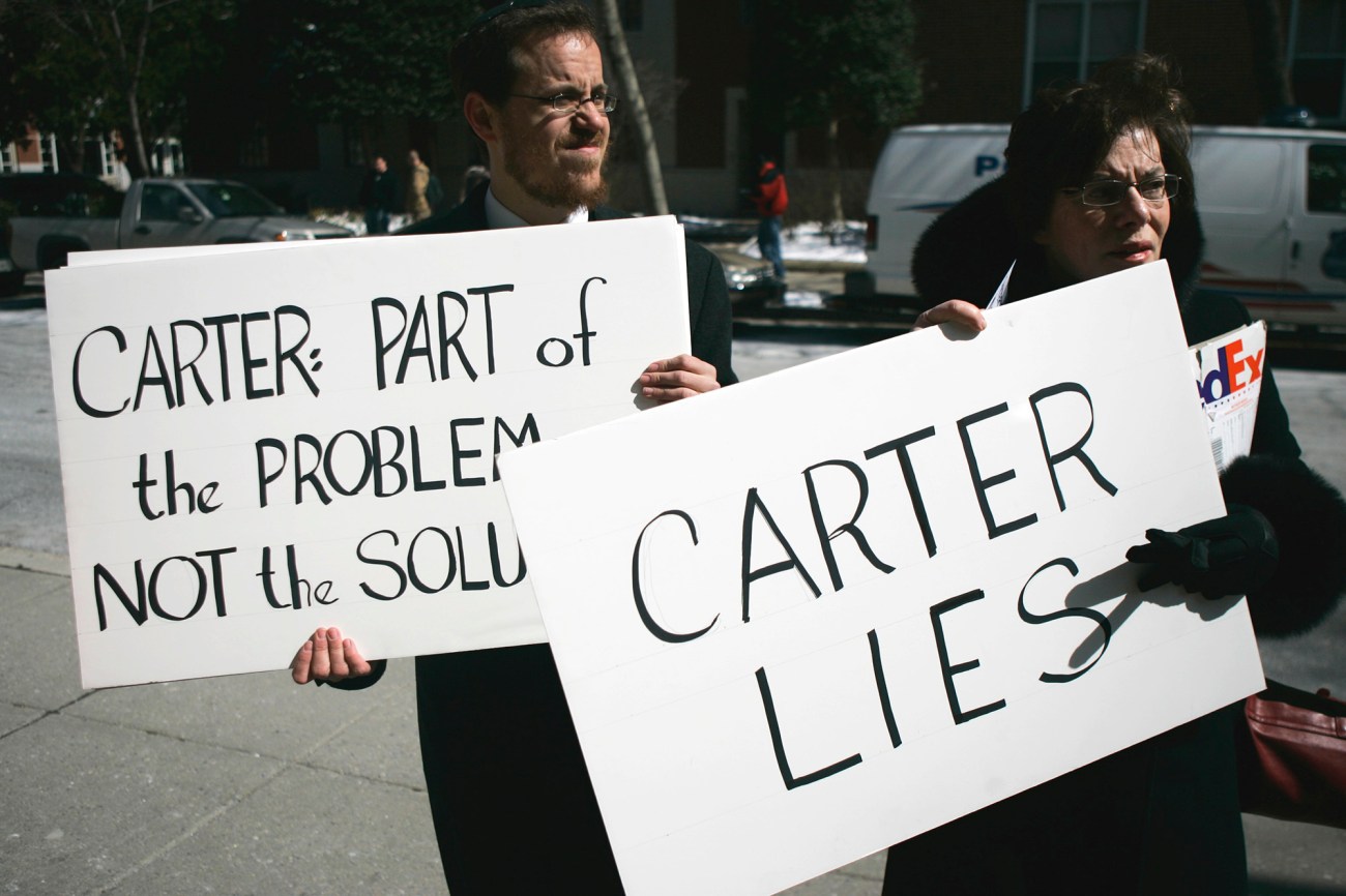 A man and woman holding signs. One reads, "Carter: Part of the Problem, not the solution," the other "Carter Lies."