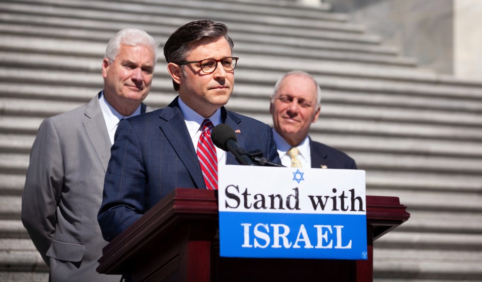 Mike Johnson in front of a podium that says "Stand with Israel"