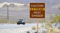 A brown sign reading CAUTION EXTREME HEAT DANGER in the desert near Death Valley, California.