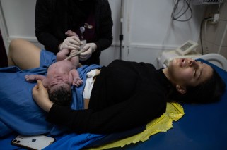 Woman laying on a hospital bed after giving birth. Her newborn is laying on her stomach, a midwife unwrapping the umbilical cord.