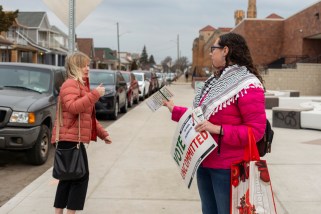 A woman in a keffiyeh offers a 'vote uncommitted' flyer to someone outside a polling place in Hamtramck, Michigan.