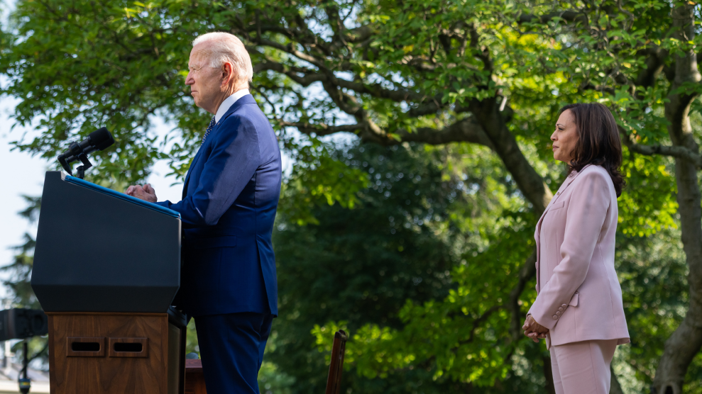 President Joe Biden stands at the presidential podium in the Rose Garden of the White House, as Vice President Kamala Harris stands a few steps behind him.
