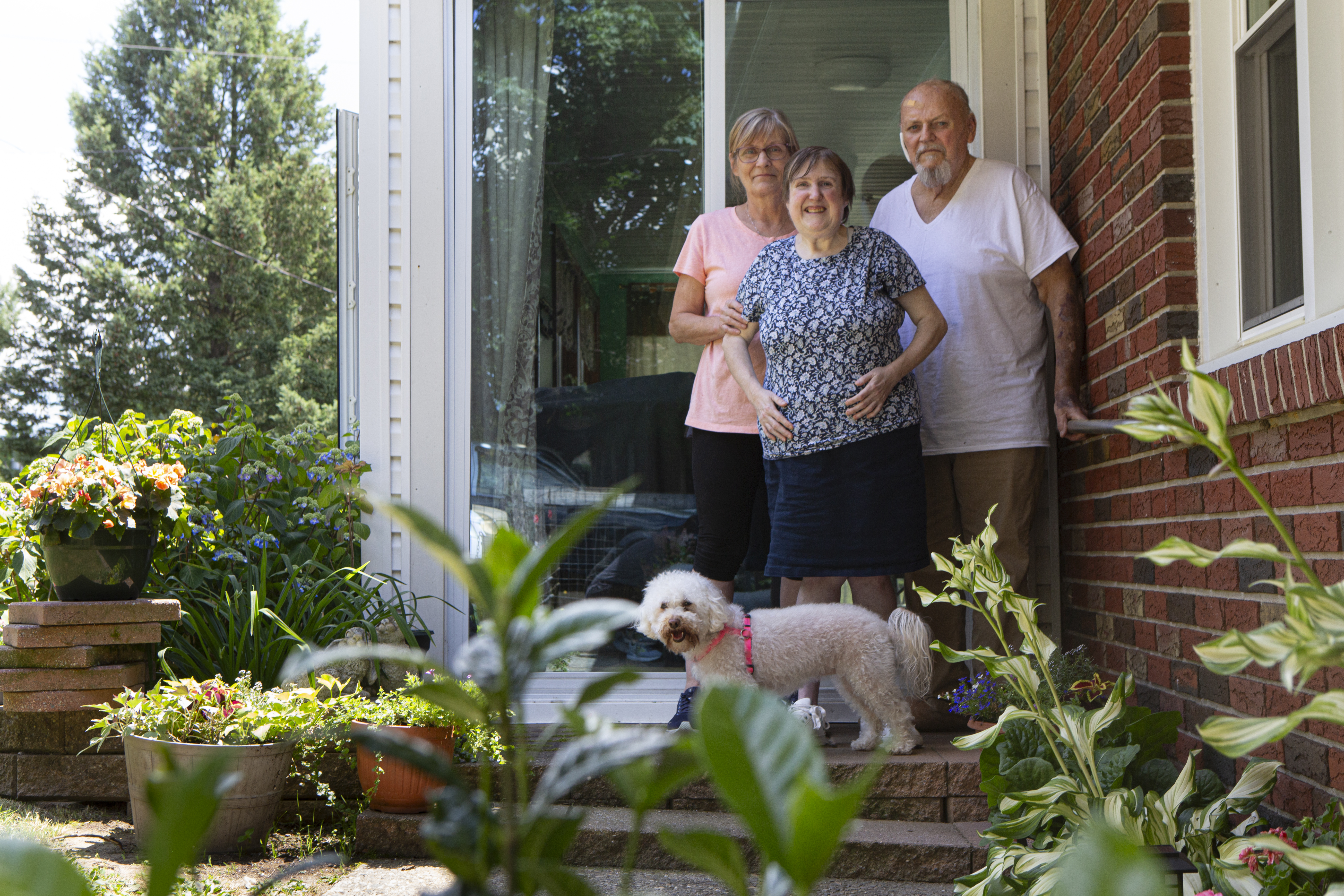 Three people and a dog standing on a porch in front of their brick house.