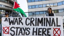 Protesters hold a sign saying "A WAR CRIMINAL STAYS HERE" outside the Watergate Hotel.