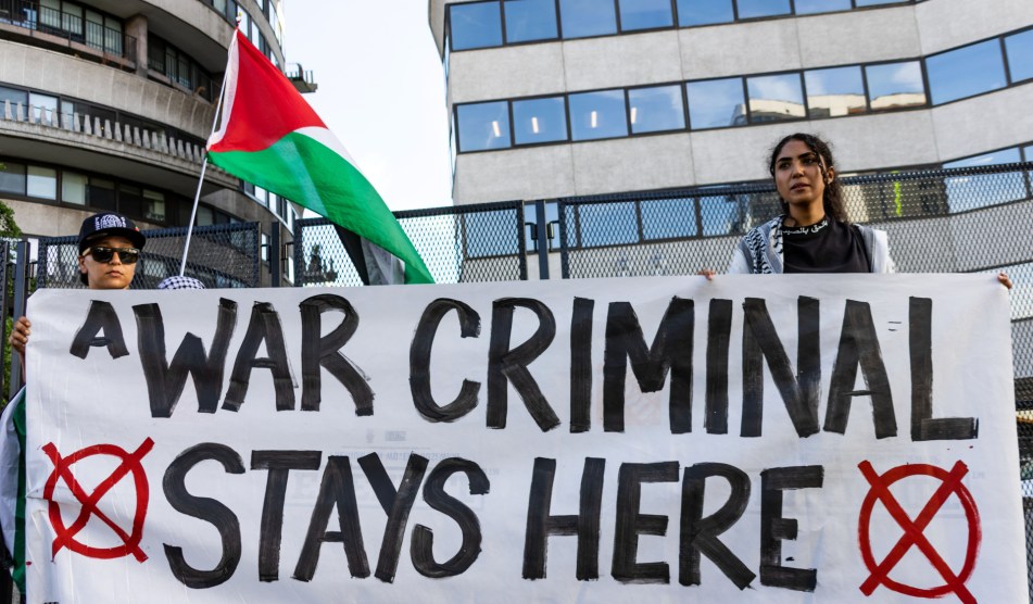 Protesters hold a sign saying "A WAR CRIMINAL STAYS HERE" outside the Watergate Hotel.