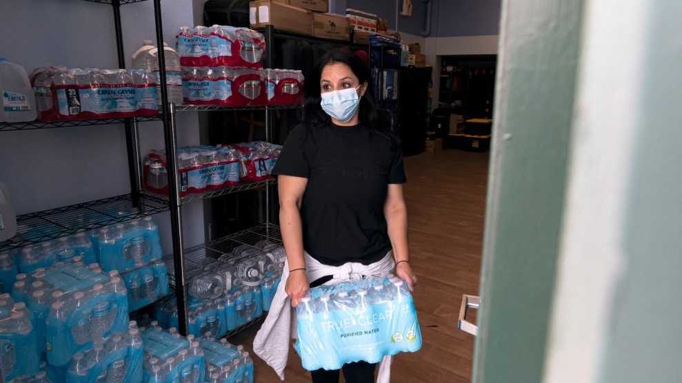 A woman wearing a surgical mask hands out water cases.