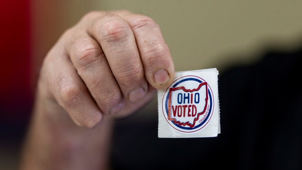 A white hand holding up a sticker that says "Ohio Voted"