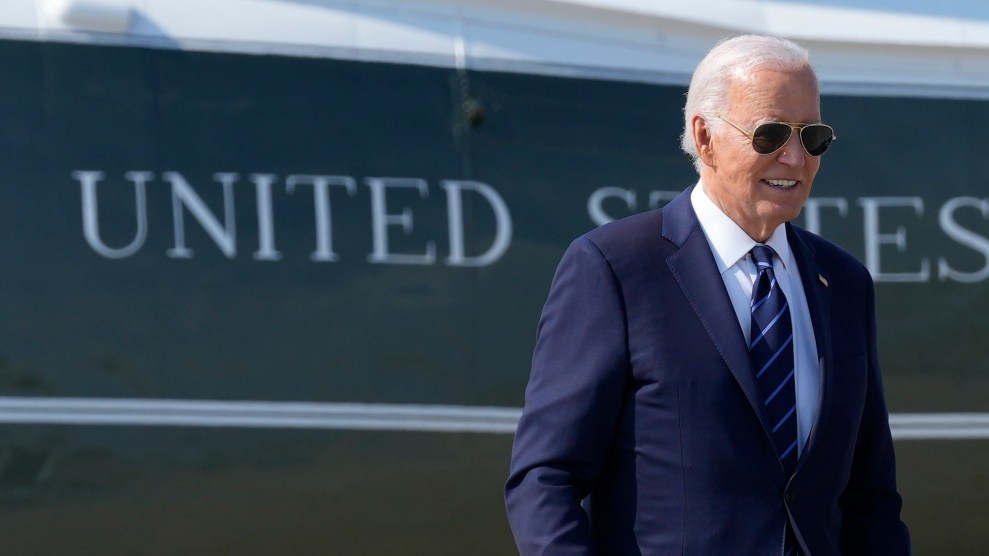 Joe Biden in a suit and sunglasses with a sign that says "United States" behind him