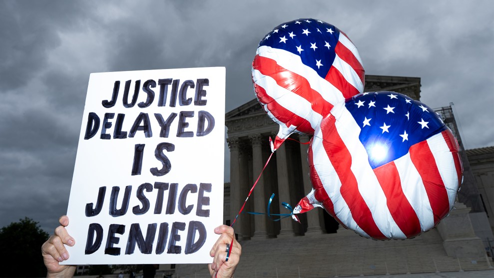 A protester holds a sign that reads "JUSTICE DELAYED IS JUSTICE DENIED" and American flag balloons in front of the Supreme Court.