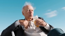 Peter Singer sits in a chair drinking through a straw.