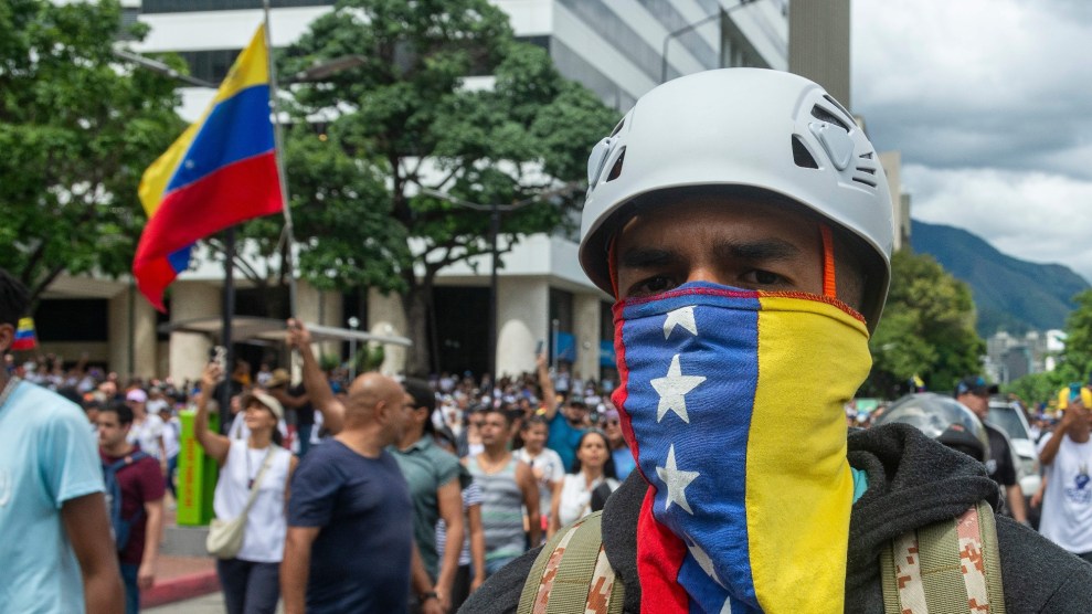 A helmeted protestor with a cloth resembling Venezuela's flag covering his face.