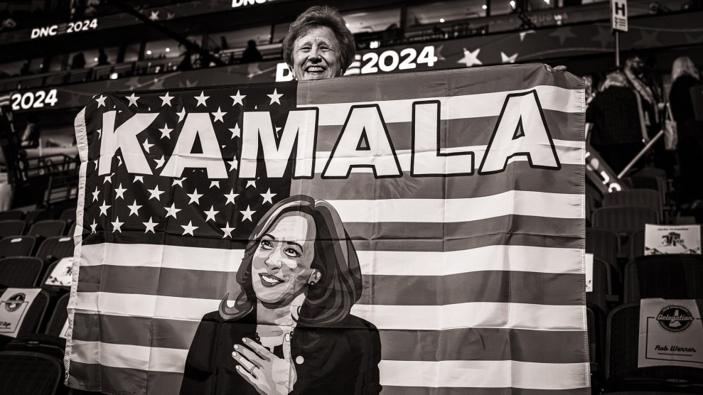 Black and white photo of a smiling woman holding an American flag that says "Kamala" at the top with an image of Vice President Kamala Harris on it.