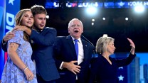 Tim Walz expresses a show of gratitude for the audience's reaction, as his wife waves and his two children standing to his right hug.