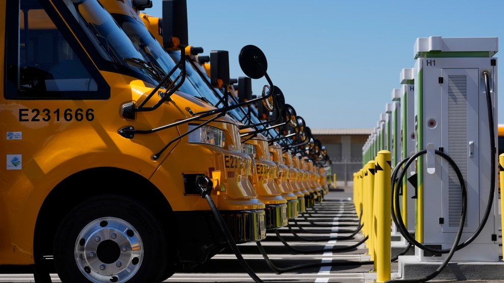 A line of yellow electric school buses plugged into their chargers.