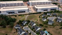 A giant data center consisting of four white blocky buildings abutting a piece of land with two residential cul-de-sacs with identical-looking white houses.