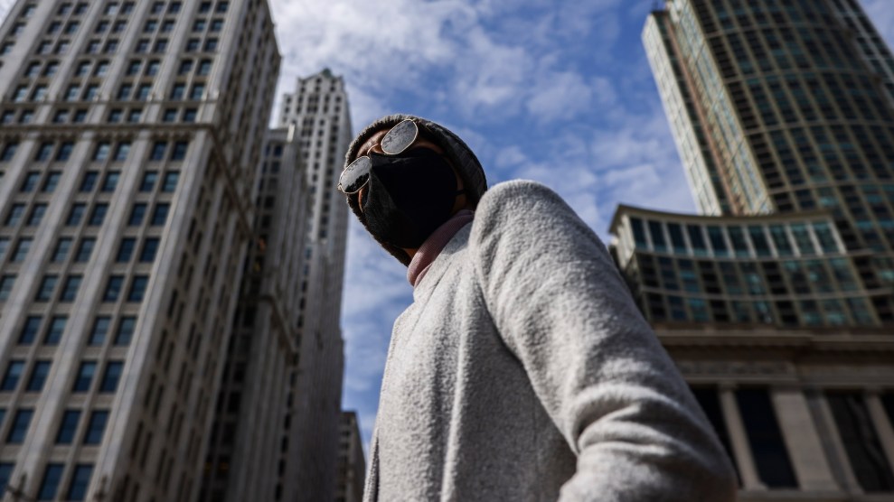 A black person wearing a black mask walks outside, surrounded by tall buildings.