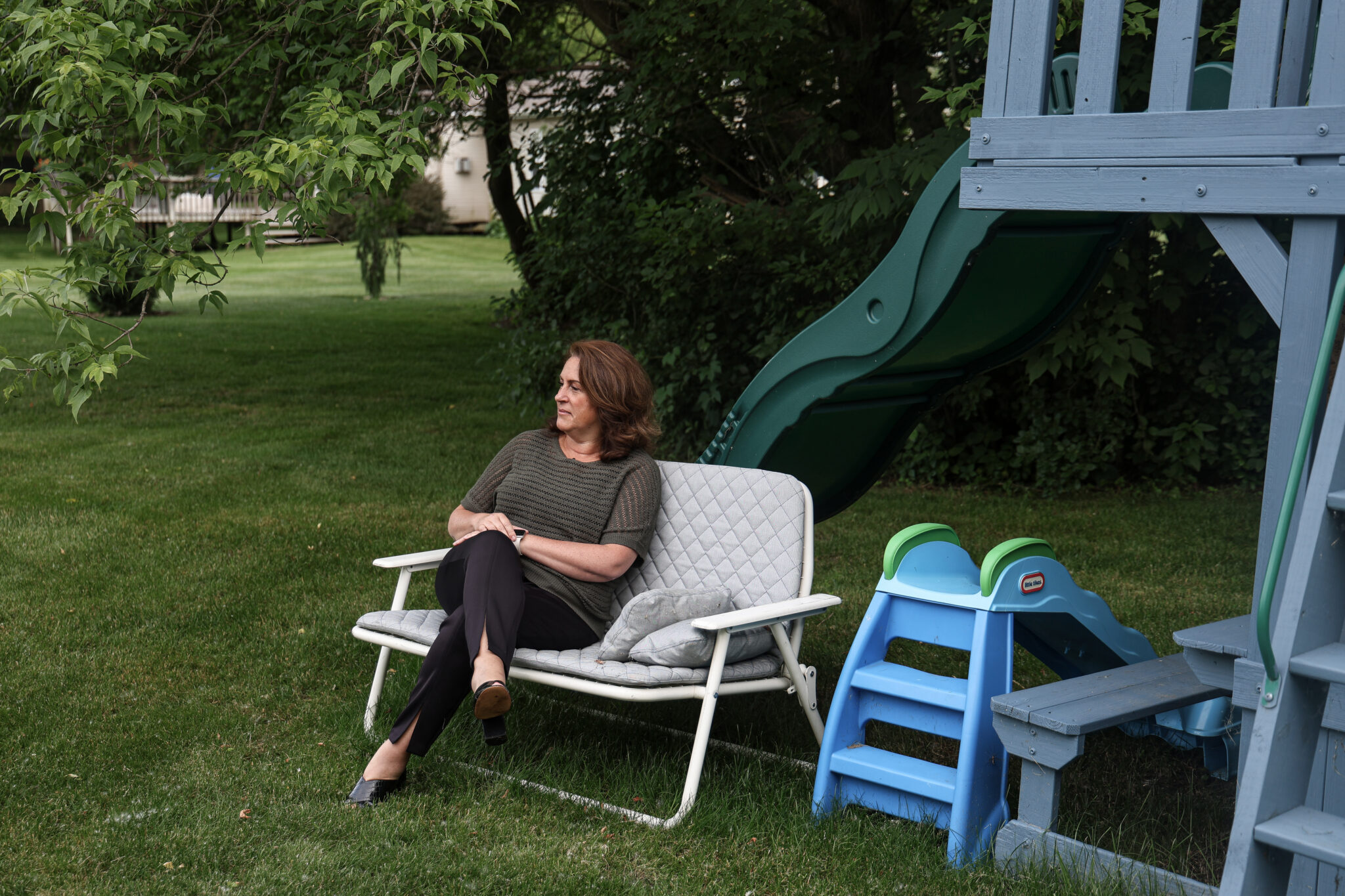 A woman sits on a folding chair on a green lawn.