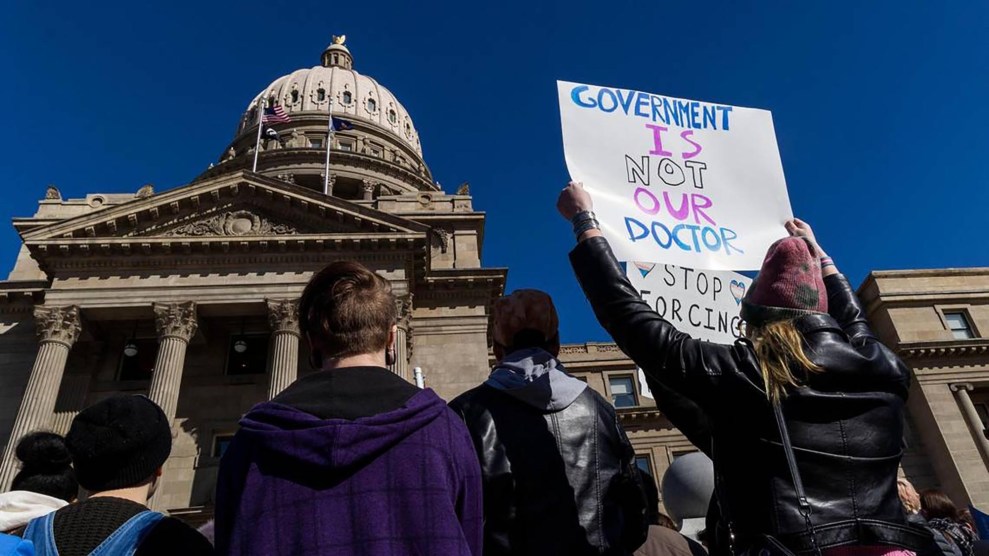 A group of protesters stand outside the Capitol building in Idaho while holding signs, one of which says, "Government is not our doctor."