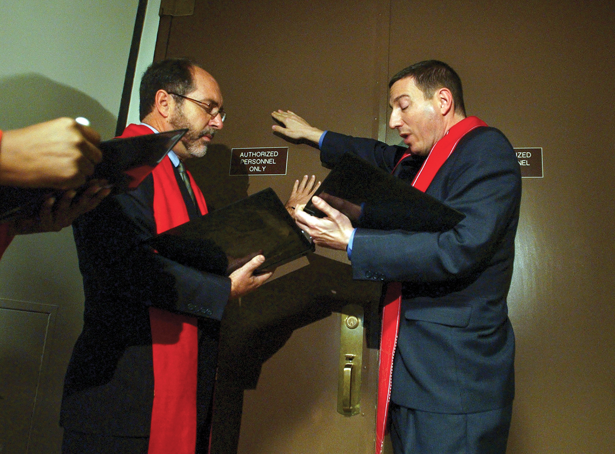 Two men holding Bibles, praying with their hands on a door.