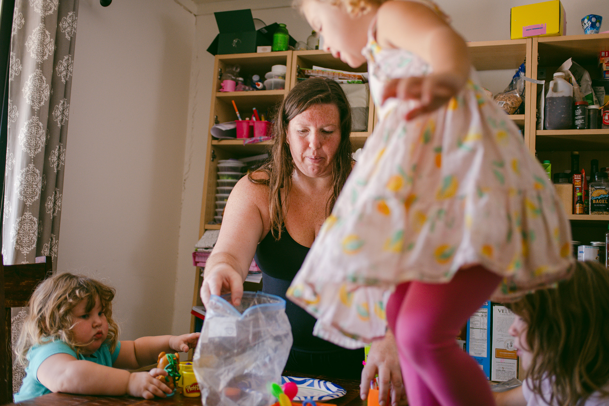 A white woman wearing a black tank top arranges her children’s toys on top of a table.