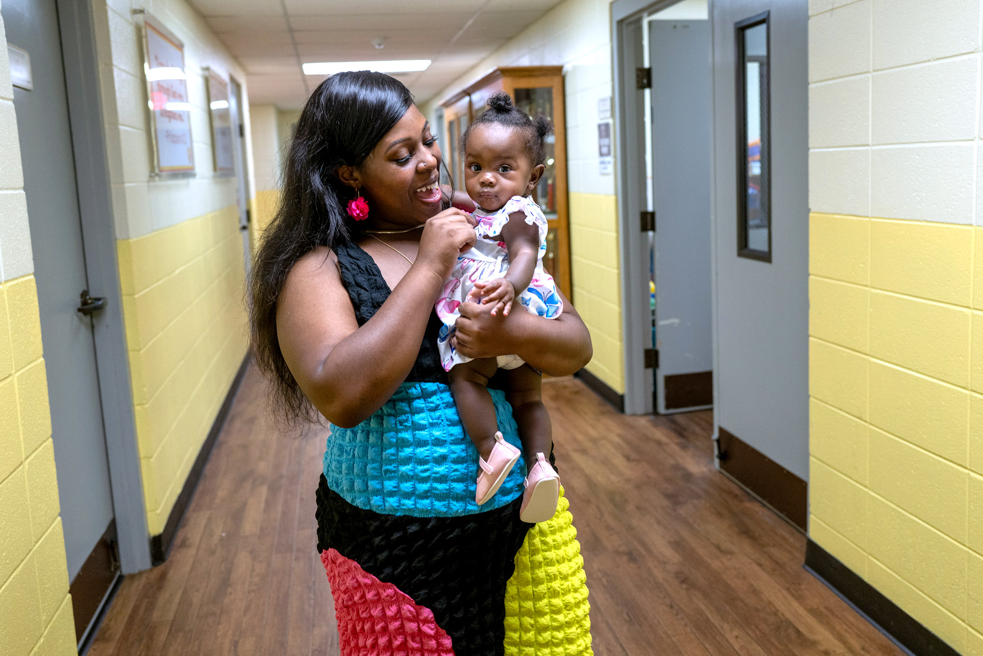 Melissa Robinson, wearing a teal blue, magenta, black-and-yellow dress, smiles as she holds her daughter.