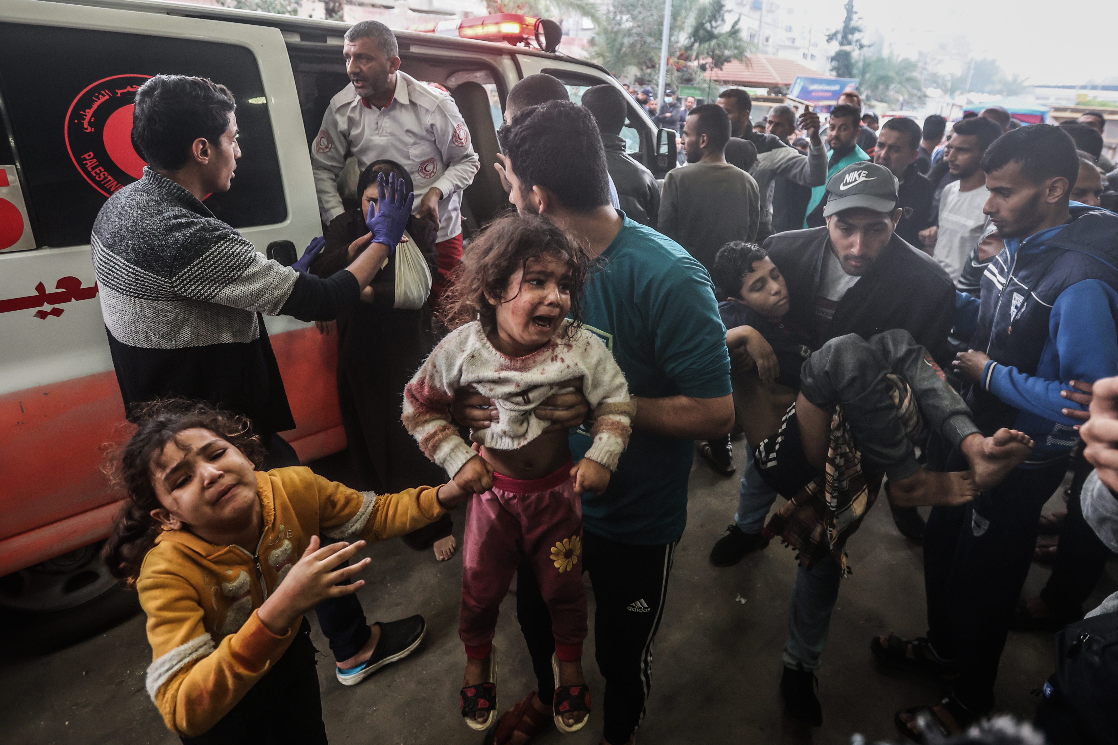 A father holds his injured daughter in a crowd outside a hospital in Gaza, while another child sobs next to him. 