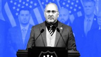 A treated photo of a man standing at a podium with American flags and onlookers behind him. The background is tinted blue.