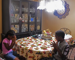 Two kids sitting at a dining room table, praying.