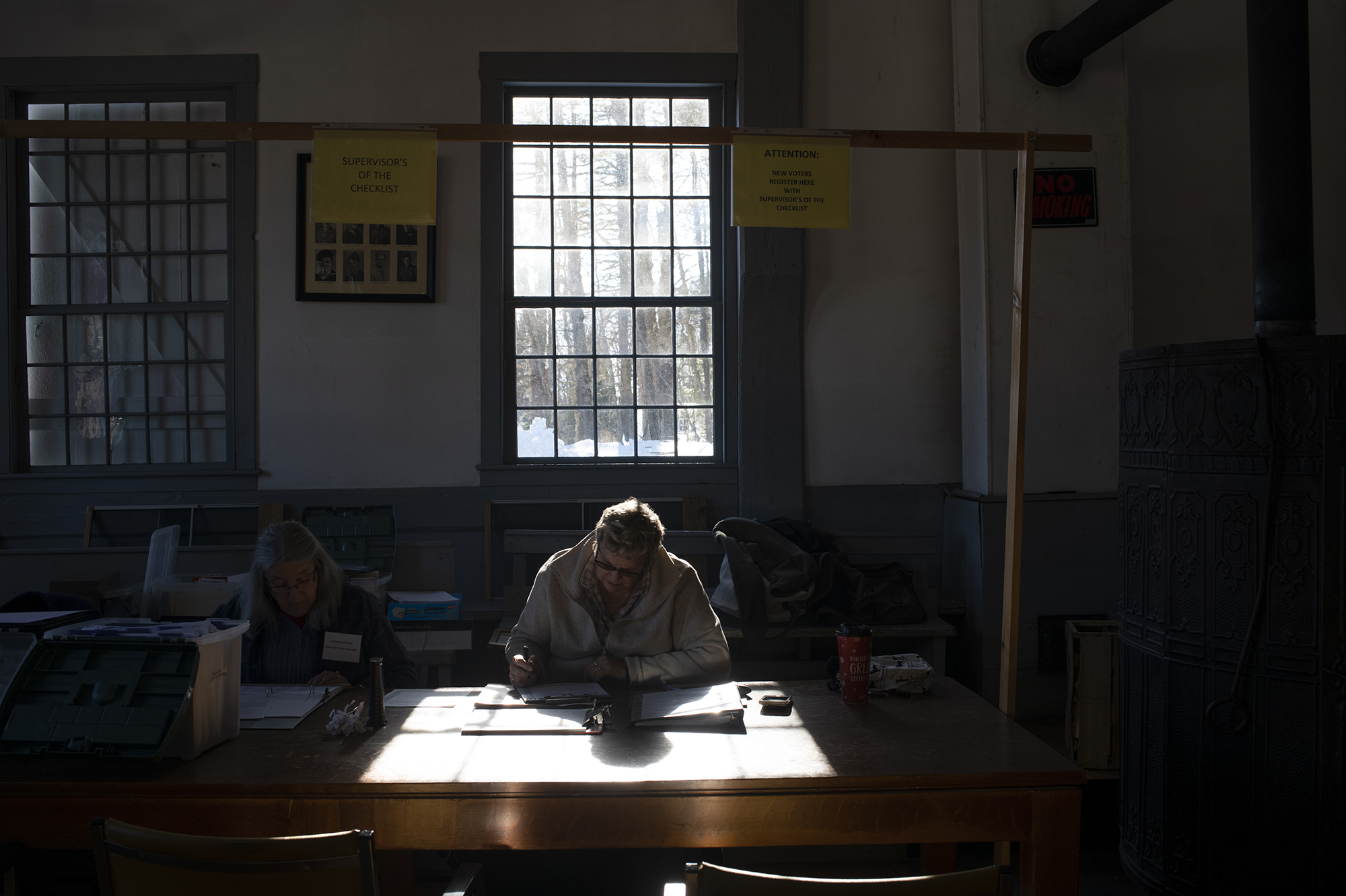 A person sits at a desk under a window in an otherwise dark room.