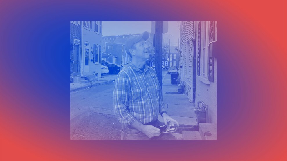 A man in front of a row of homes, canvassing. The man is wearing jeans, a plaid shirt and a baseball cap.