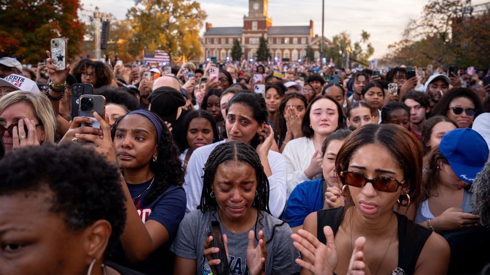 A large group of people, mostly women, stand together watching Kamala Harris speak; a young Black woman in the middle of the group is crying, and many others have tears streaming down their faces.