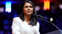 Tulsi Gabbard, wearing white jacket, speaking in front of a lectern