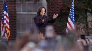 Kamala Harris stands at a podium in front of a crowd of supporters. Behind her are American flags.