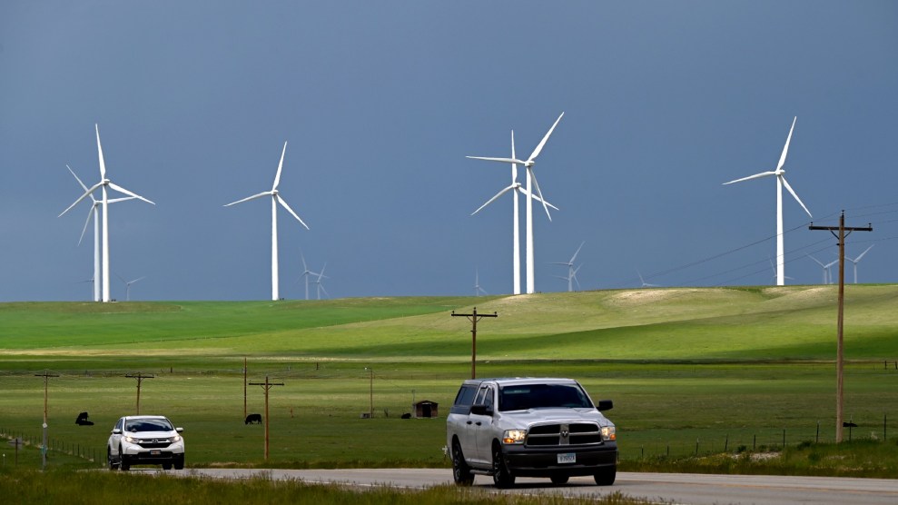 A few car drive on a road with a backdrop of multiple white, windmills spinning