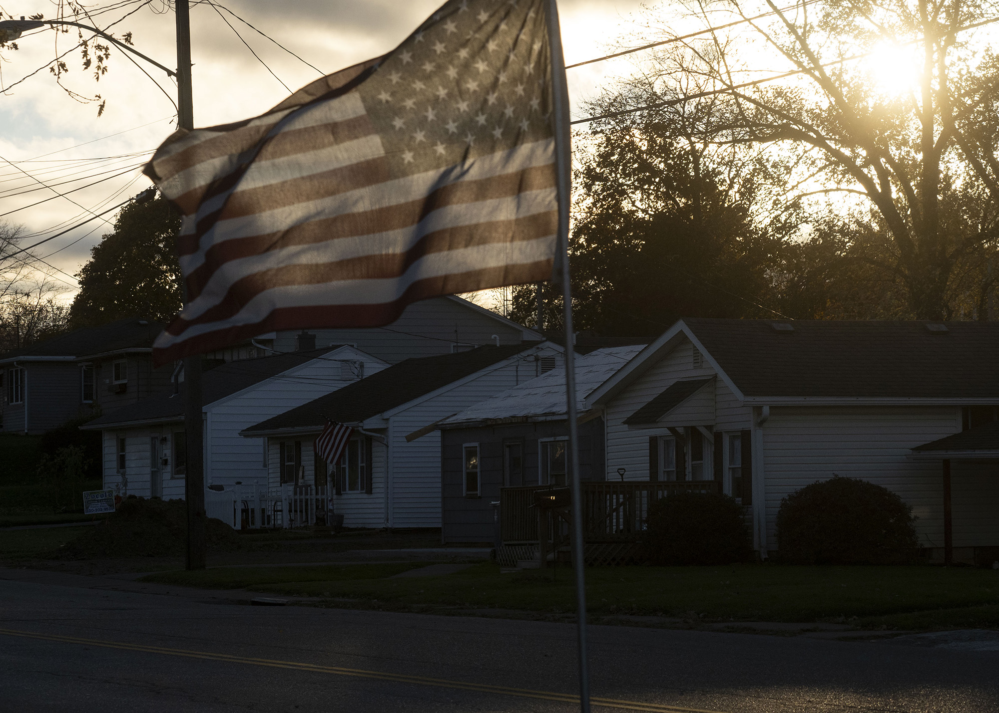 An American flag flying as the sun rises over a neighborhood.