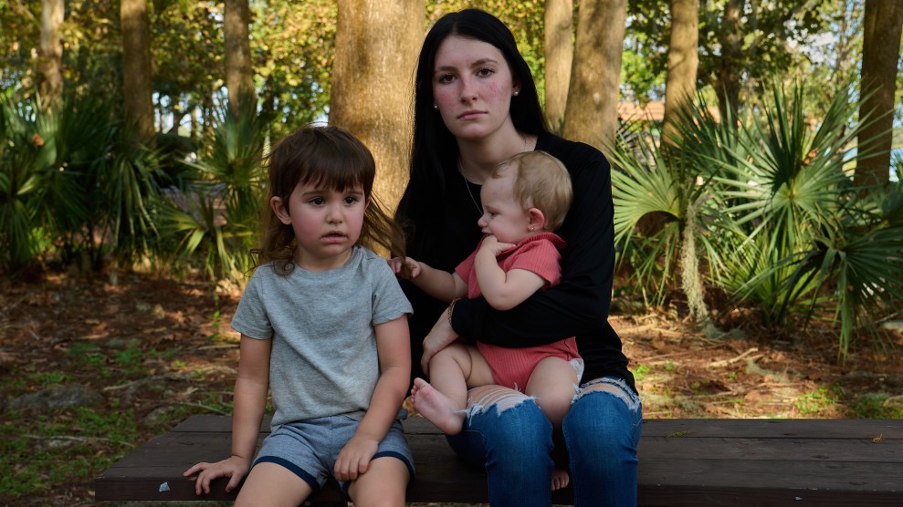 Woman sitting outside on a bench with a child in her lap and another child sitting next to her.