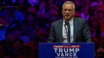 Robert Kennedy speaking behind a podium bearing a Trump-Vance sign.