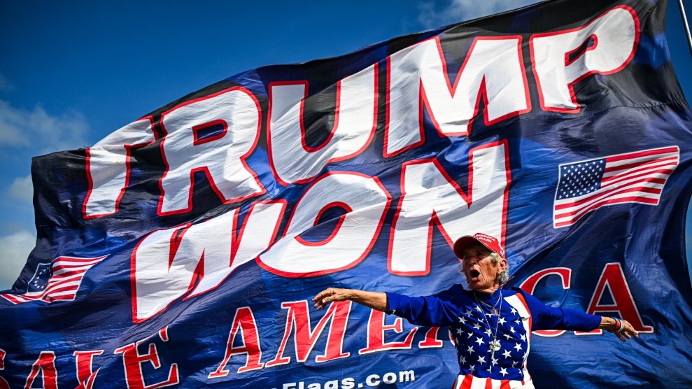 A woman in a US flag clothes stands in front of a massive flag that says Trump Won