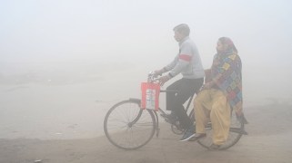 Two people on a bike are partially visible through thick air pollution