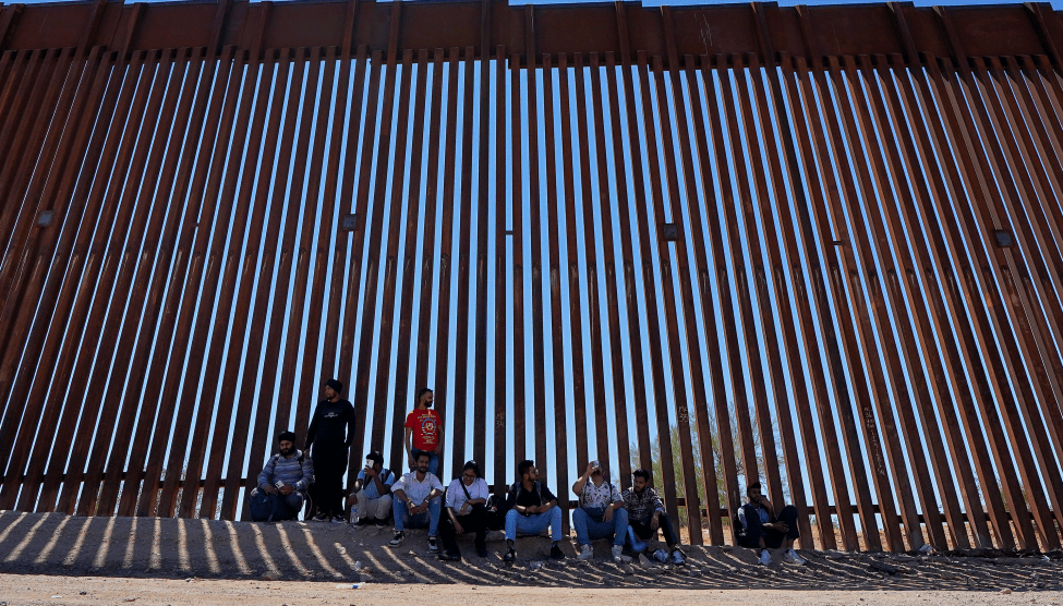 A group of 10 people sit in front of the Tucson, Arizona, section of the US-Mexico border.