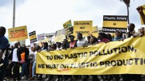 a group of protestors hold yellow signs about plastic crisis and pollution