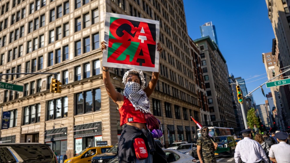 girl holds a sign reading "Gaza" with a keffiyeh covering her face.