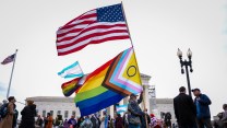 A rallygoer waves giant LGBTQ and American flags in front of the Supreme Court.