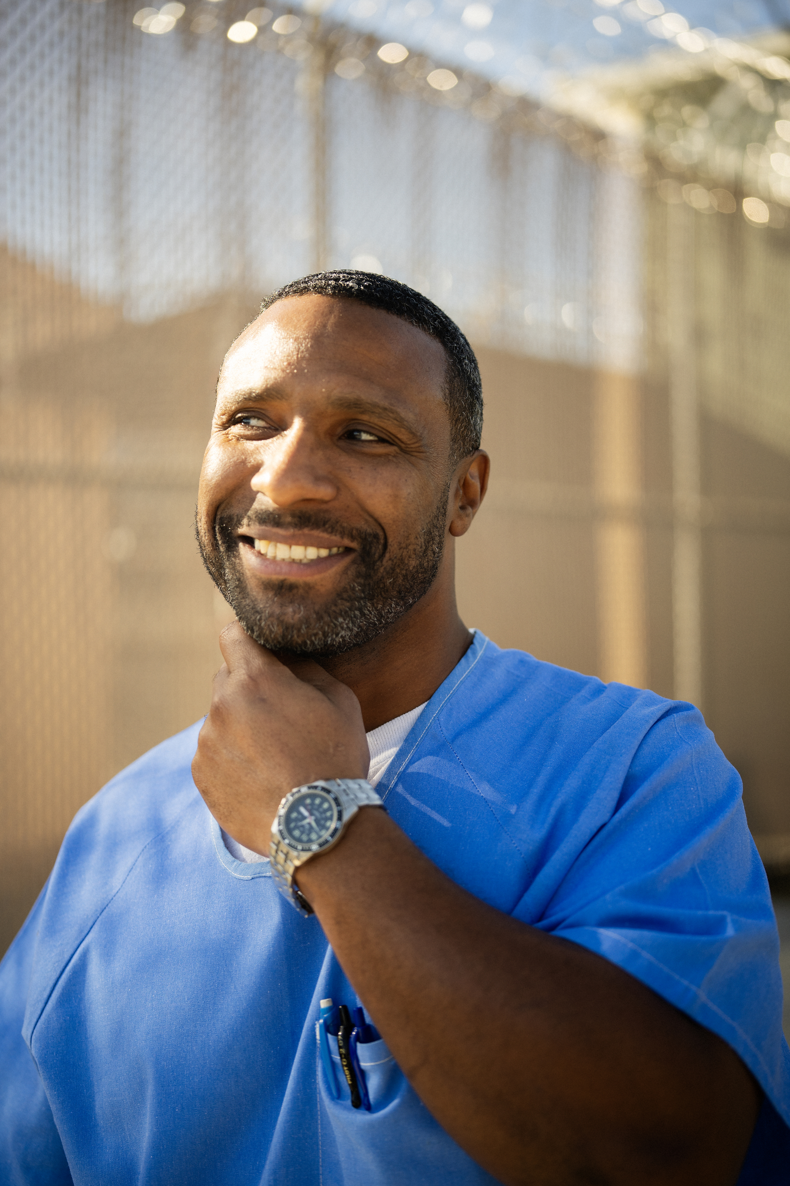 Portrait of smiling black man wearing blue with his hand on his neck.