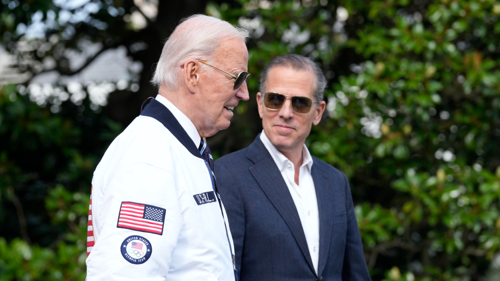 Hunter Biden wearing a suit looks at Joe Biden wearing a Team USA jacker with a slight smile.