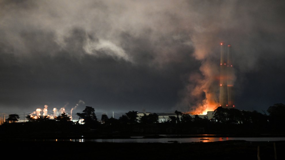 A power plant fire lights up a cloudy sky at a power plant whose tall towers have lights to keep airplanes from hitting them.