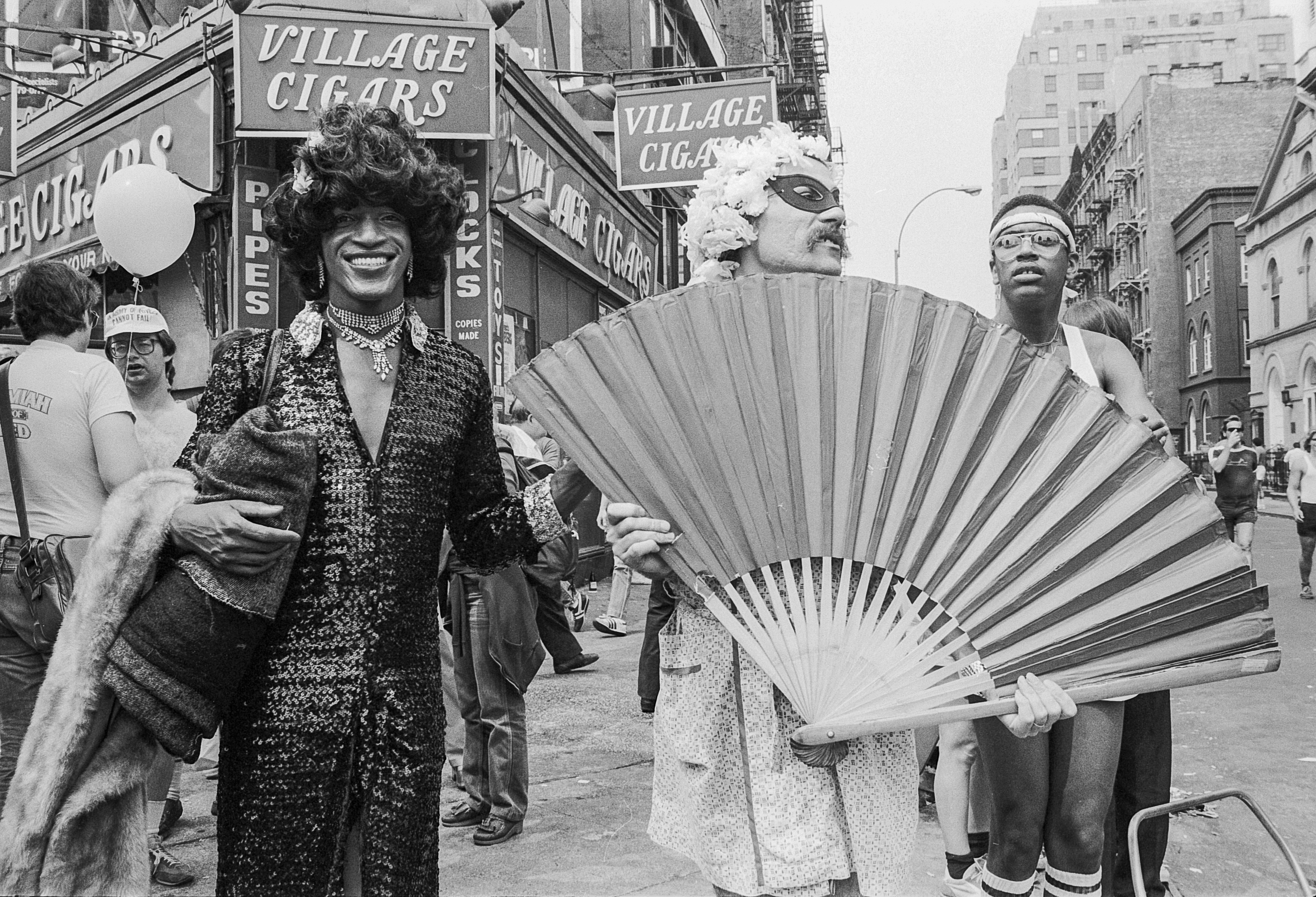 A black woman smiles next to a white person holding a huge fan.