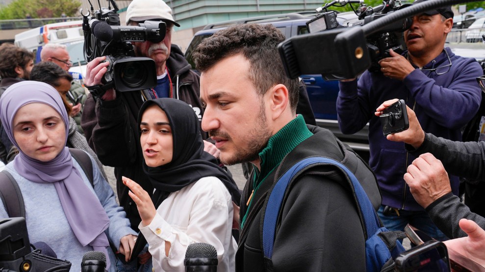 Man surrounded by media cameras and microphones.